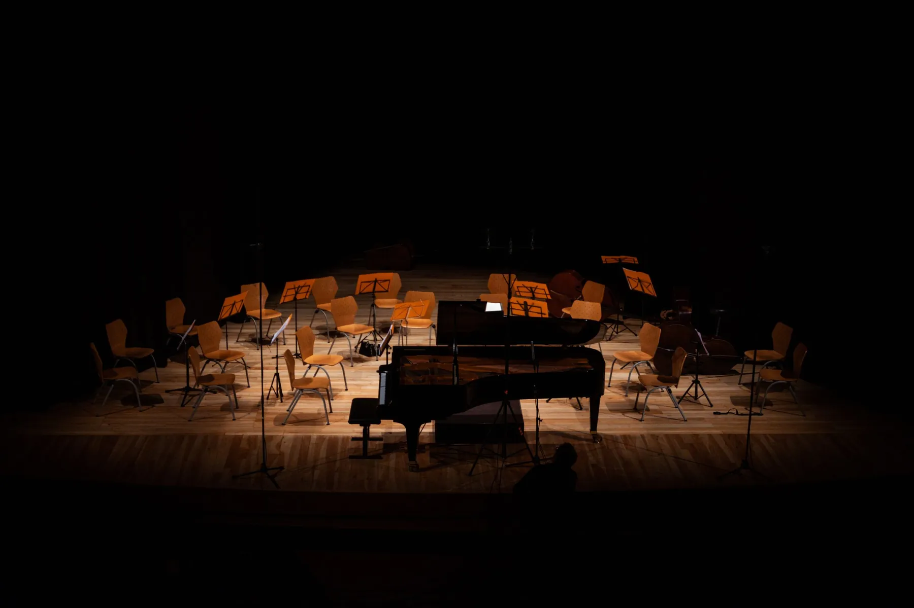 Klavír na ztemnělém pódiu, židle a stojany na noty čekají na koncert