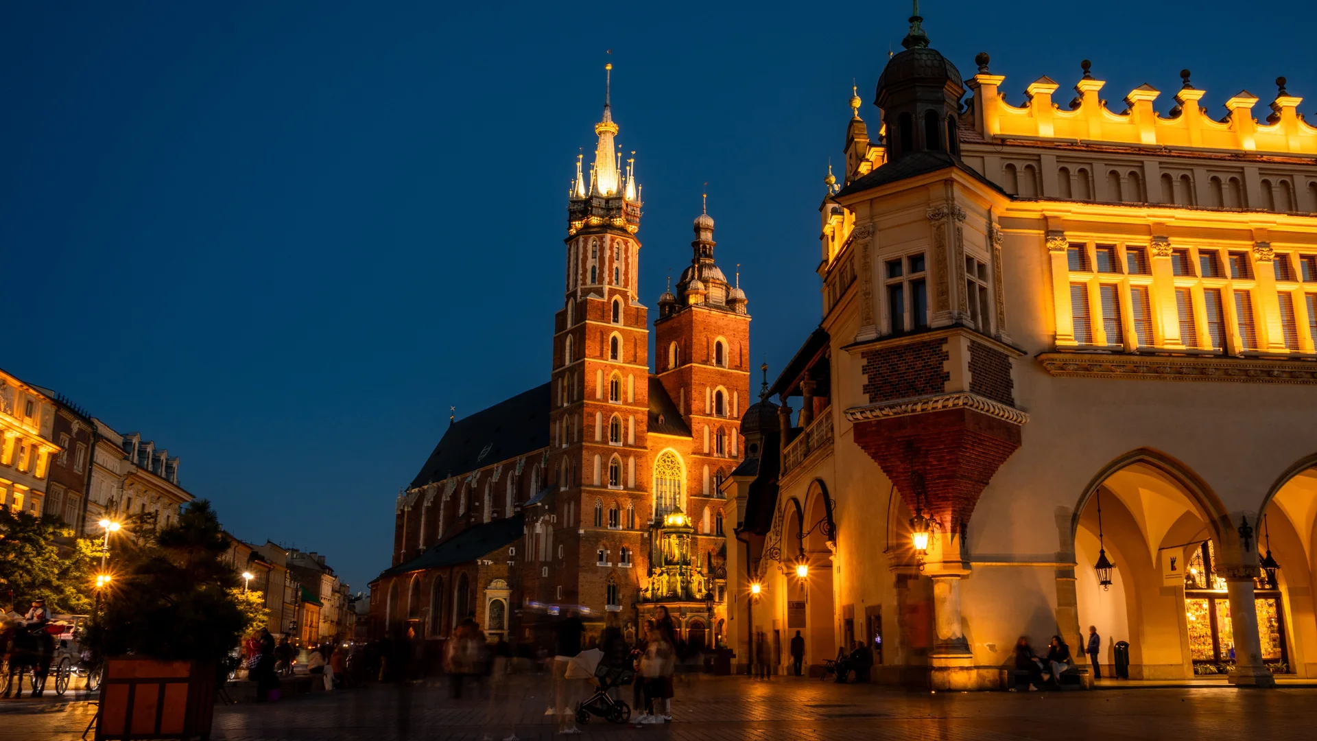 Die Marienbasilika und die Tuchhallen am Krakauer Hauptmarkt zur blauen Stunde, golden erleuchtet vor tiefblauem Himmel